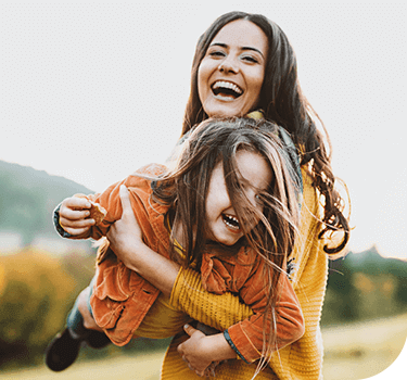 Fotografía de una mujer cargando a una niña, ambas sonríen.